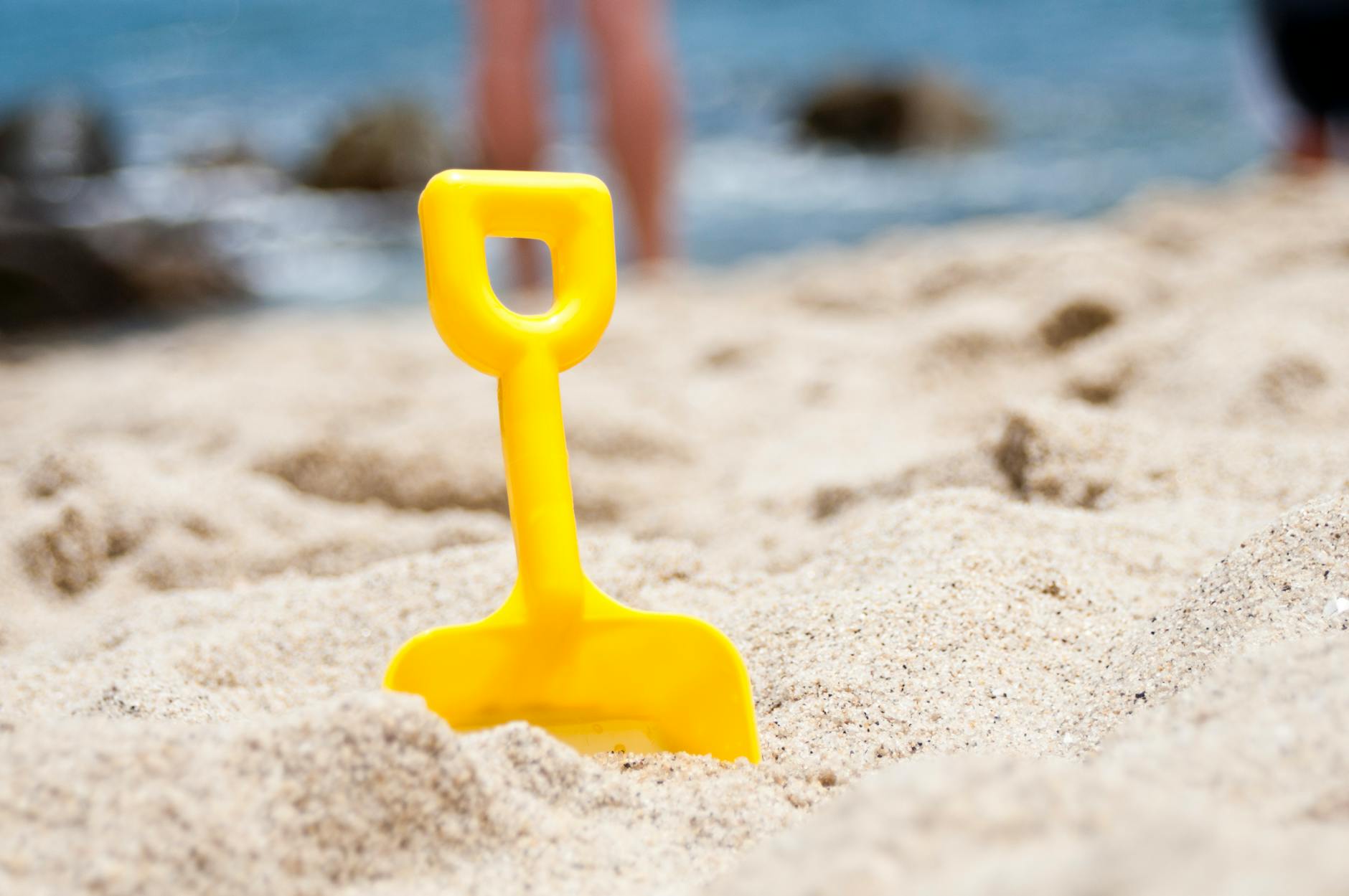 yellow shovel half buried on sand near the ocean