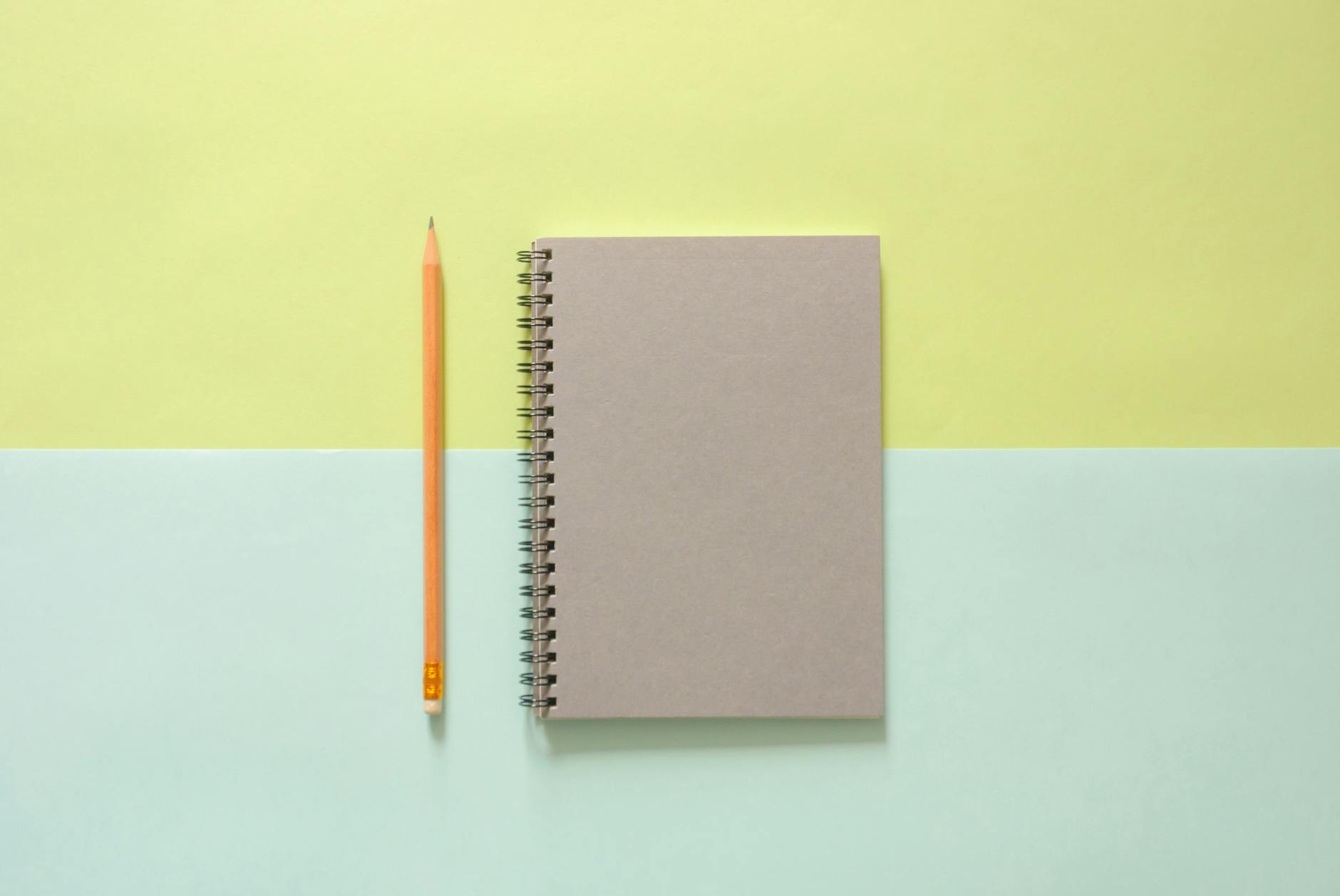 white spiral notebook beside orange pencil