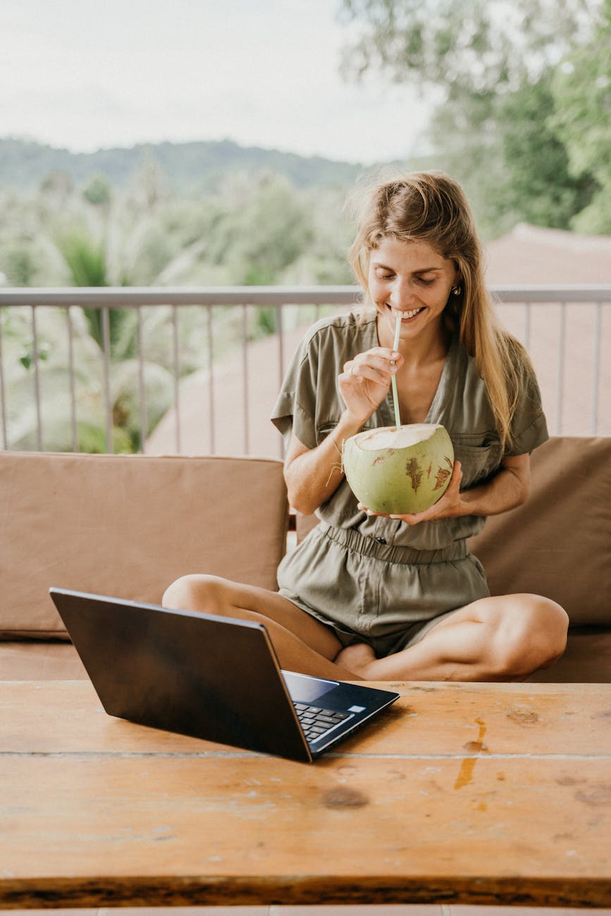 happy woman drinking coconut juice while in front of a laptop